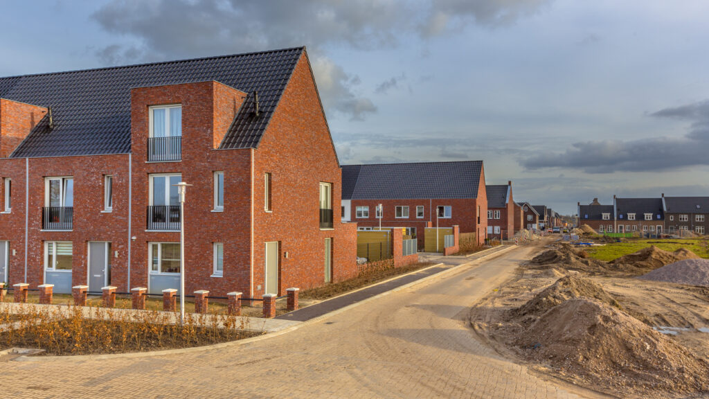 A row of contemporary brick houses under construction in a new residential estate, featuring unfinished roads and building sites, illustrating property development and housing expansion.