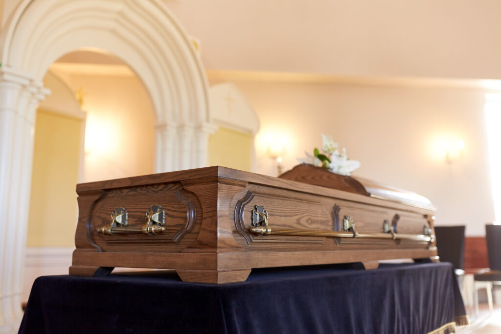 A wooden funeral casket displayed on a table during a memorial service, with soft lighting and elegant decor in the background.