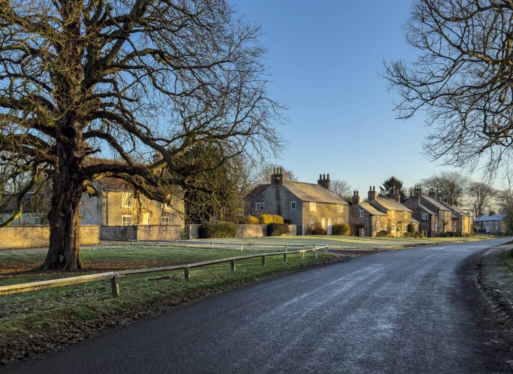 Charming rural street scene featuring traditional stone cottages and a quiet road, illustrating property values and buyer offers below asking price in rural areas.