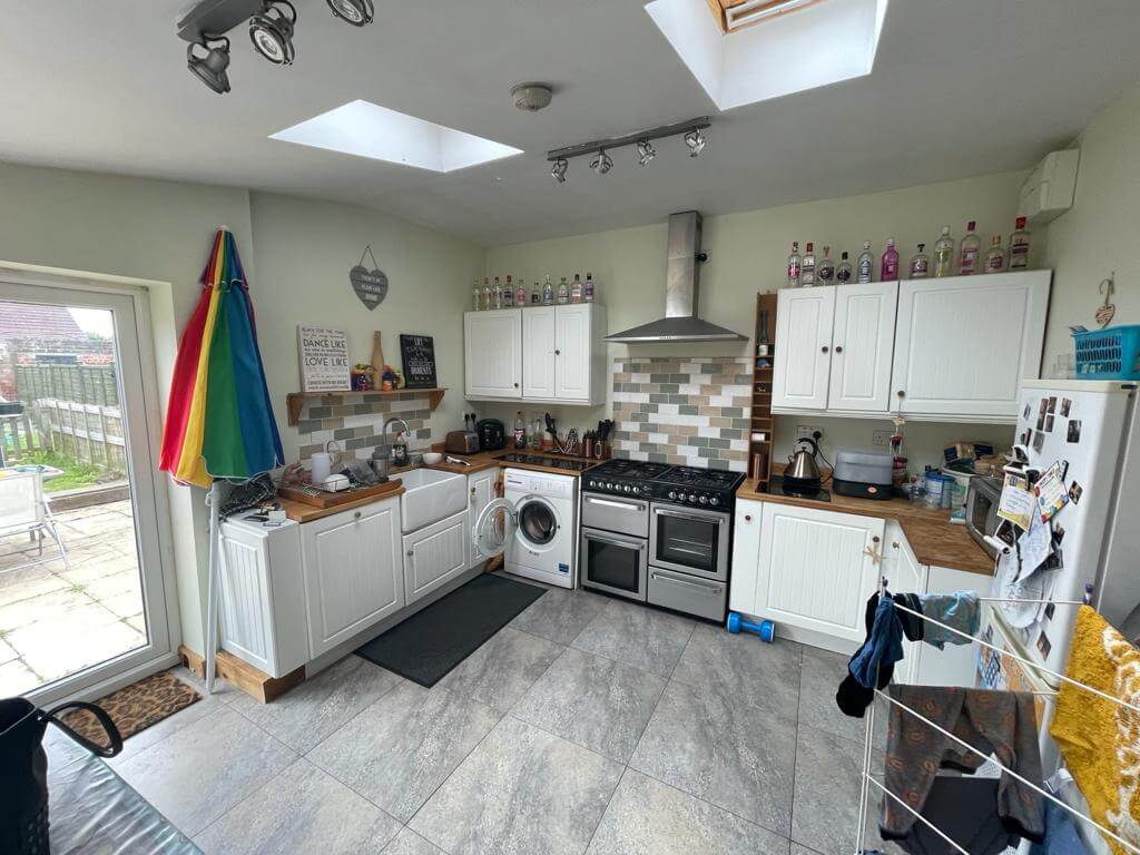 Bright modern kitchen with white shaker cabinets, tiled backsplash, skylight, and appliances; perfect for family living and meal preparation.