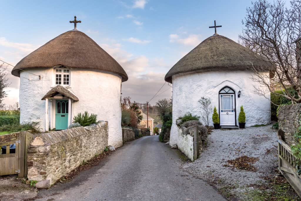 Charming white cottages with thatched roofs on a rural country road, showcasing attractive property exteriors for sale or rent, perfect for traditional English countryside living.