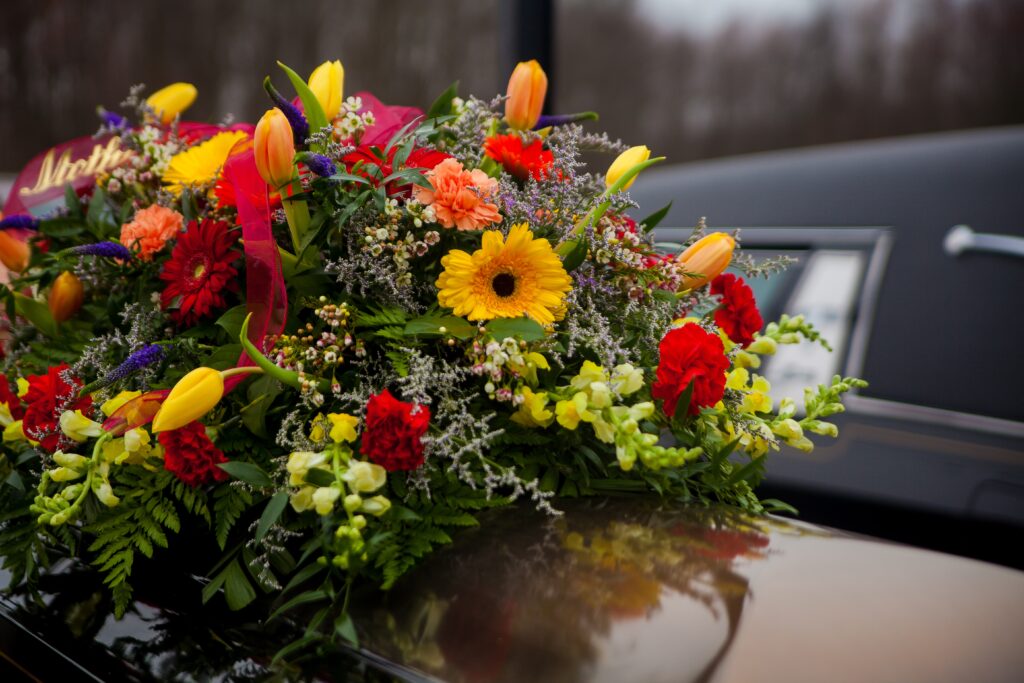 An elegant and colourful funeral flower bouquet placed on a car hood, symbolising remembrance and respect for loved ones after death.