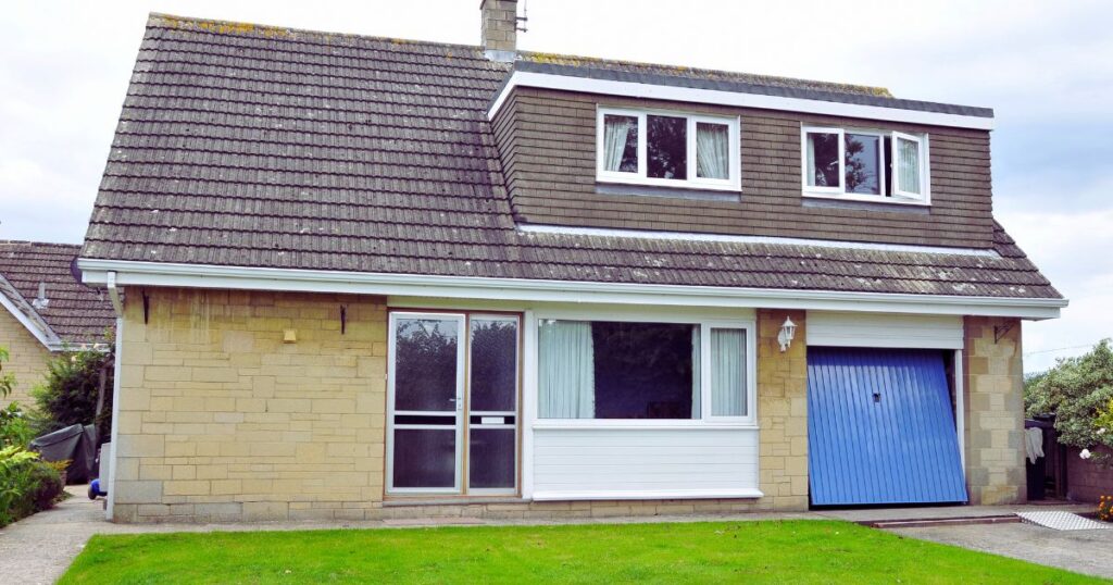 Bright, detached house with a pitched roof, large front window, and a blue garage door, showcasing home repair and maintenance services offered by Property Saviour in the UK.