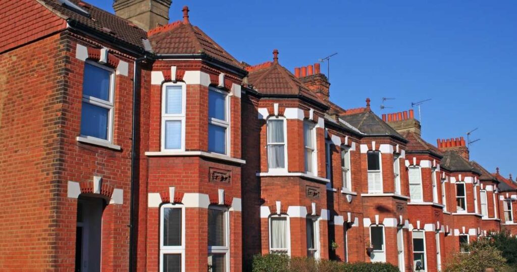 Red brick Victorian terraced houses with white window frames and decorative brickwork, under a clear blue sky, showcasing traditional UK residential architecture.