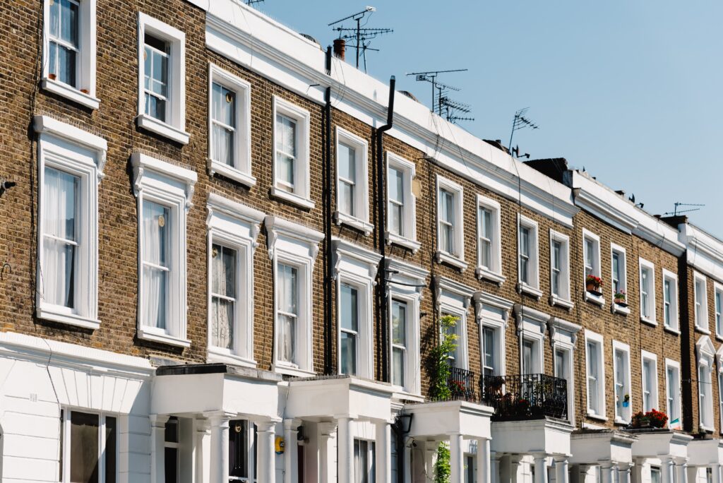 Victorian terraced houses in London with white window frames, brick façades, and adorned with flower boxes under a clear blue sky.