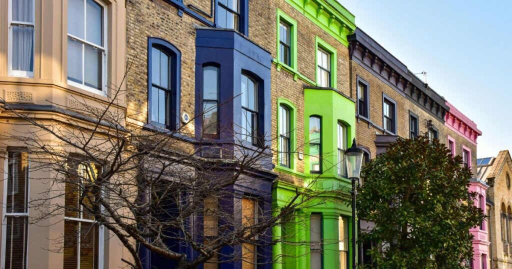 Brightly coloured Victorian terrace houses in London featuring bold blue, green, pink, beige, and black facades, showcasing vibrant architectural styles in an urban setting.