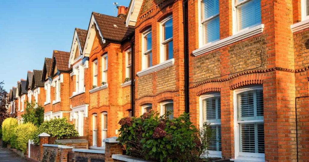 Victorian red brick terrace houses with white window frames and decorative brickwork, set in a sunny residential neighbourhood with lush greenery and classic architectural details.