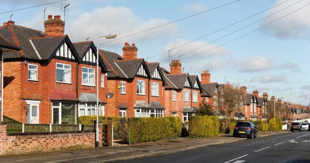 Red brick houses with black and white timber accents along a suburban street, showcasing typical residential architecture and well-maintained gardens.
