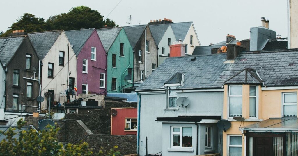 Colourful terraced houses on a hillside in a residential neighbourhood, showcasing diverse architecture and vibrant exterior paintwork. This image highlights typical UK housing with satellite dishes and varied roof styles.