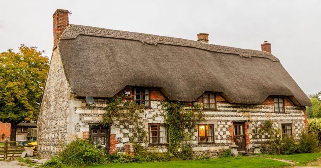 Charming traditional cottage with a thatched roof, brick and flint walls, and lush garden, perfect for property maintenance and restoration services.