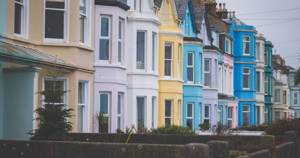 Bright coloured Victorian terraced houses in a seaside UK town, showcasing vibrant pastel facades, bay windows, and traditional architecture, offering potential homeowners an attractive colonial-style property.