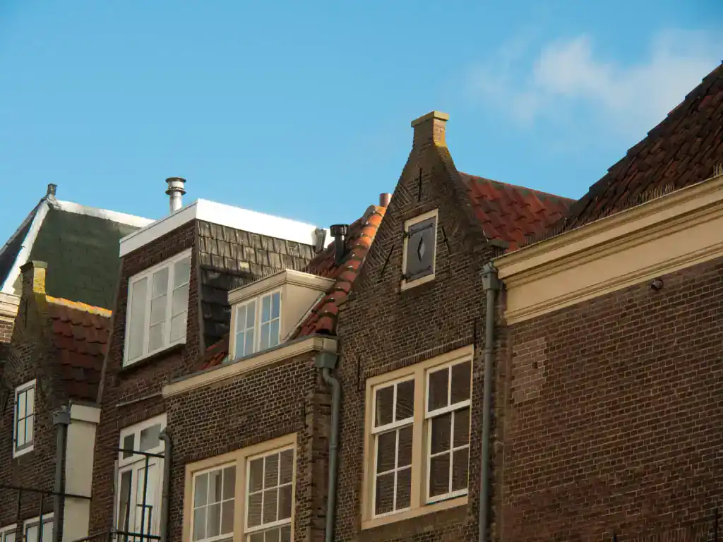Charming brick townhouses with steep gabled roofs under a clear blue sky, featuring multiple chimneys and white-framed windows.