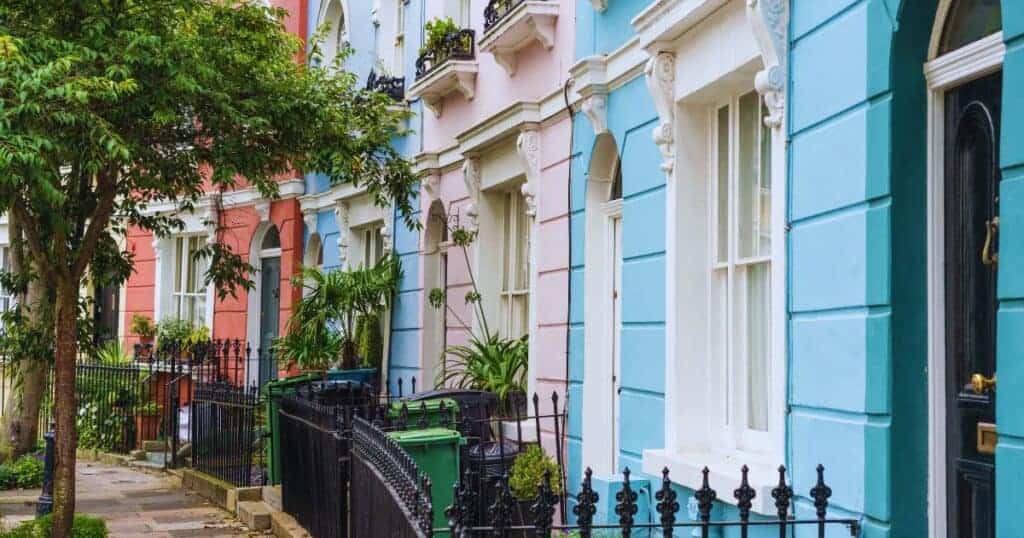 Vibrant colourful Victorian townhouses in pastel shades with decorative architecture, green garden plants, and a black wrought iron fence, showcasing charming residential property exteriors.
