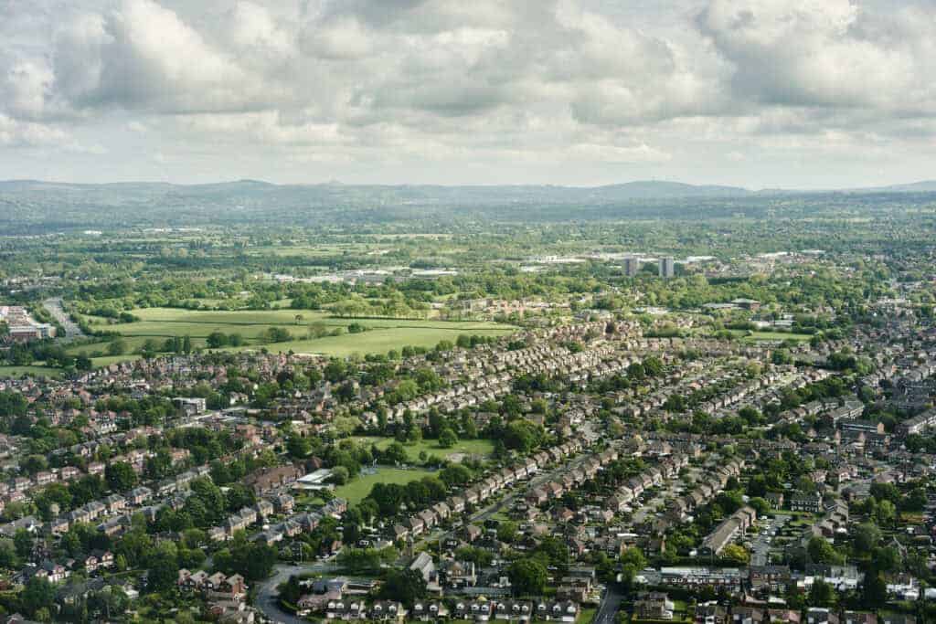 Sprawling aerial view of a suburban residential area surrounded by lush greenery and open fields, showcasing a peaceful neighbourhood perfect for property investment and property management in the UK.