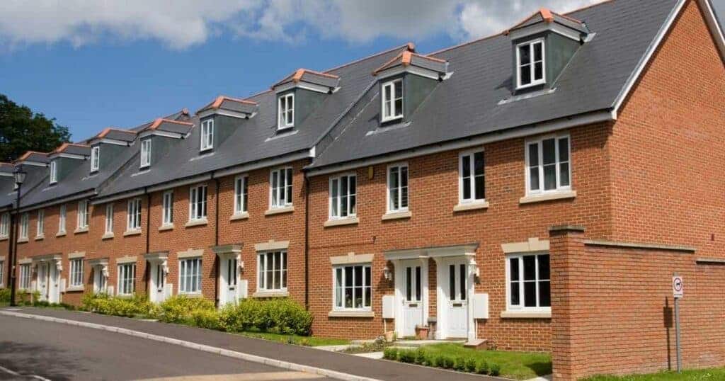 Modern residential terraced houses with brick exterior and grey sloped roofs in a suburban neighbourhood.