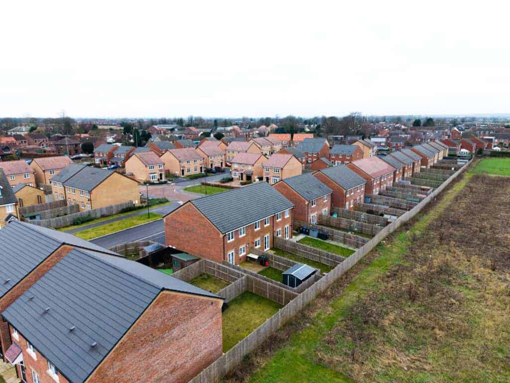 Detached modern houses with private gardens in a new suburban housing development, featuring secure fencing and well-maintained outdoor spaces.