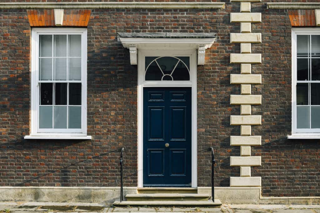 Classic Georgian façade with dark blue door and white windows, set in red brick wall with decorative stone detailing.