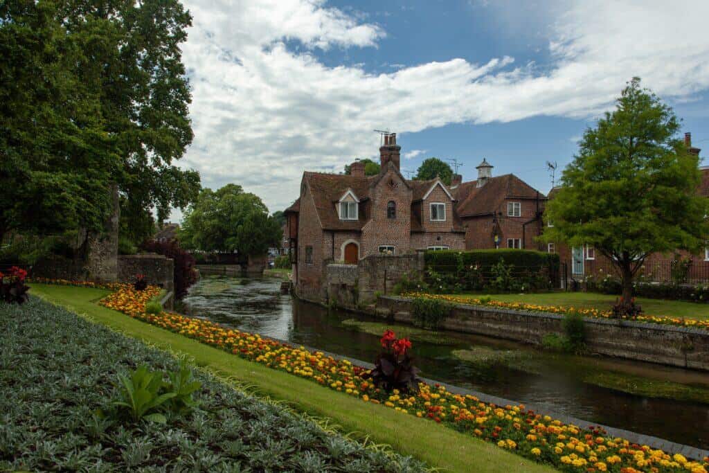 Picturesque historic house situated beside a tranquil waterway, surrounded by lush greenery and vibrant flowerbeds, illustrating the process of selling a house through probate.