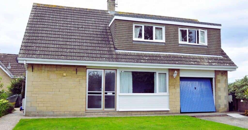 Clay brick house with blue garage door and upper floor dormer windows, front lawn, and driveway, showcasing property maintenance and repair services by Property Saviour.