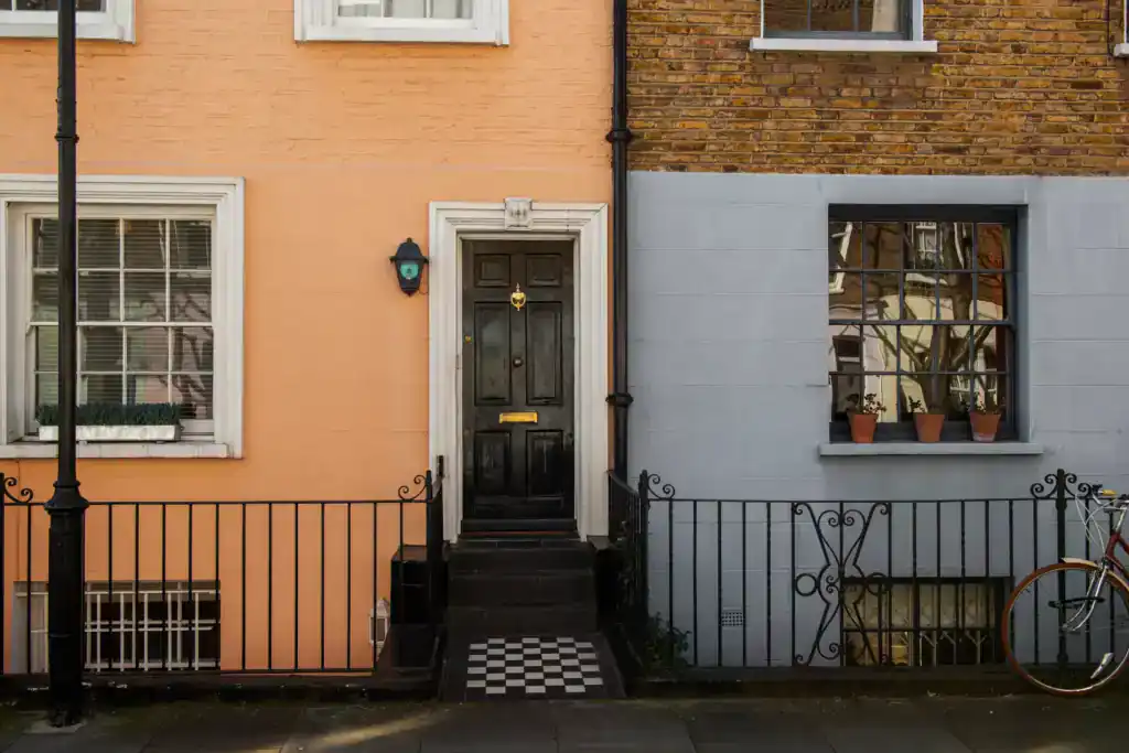 Charming UK terraced house with a black front door, white window frames, and a small front garden enclosed by a black metal fence, perfect for those inheriting a fully paid-off property.