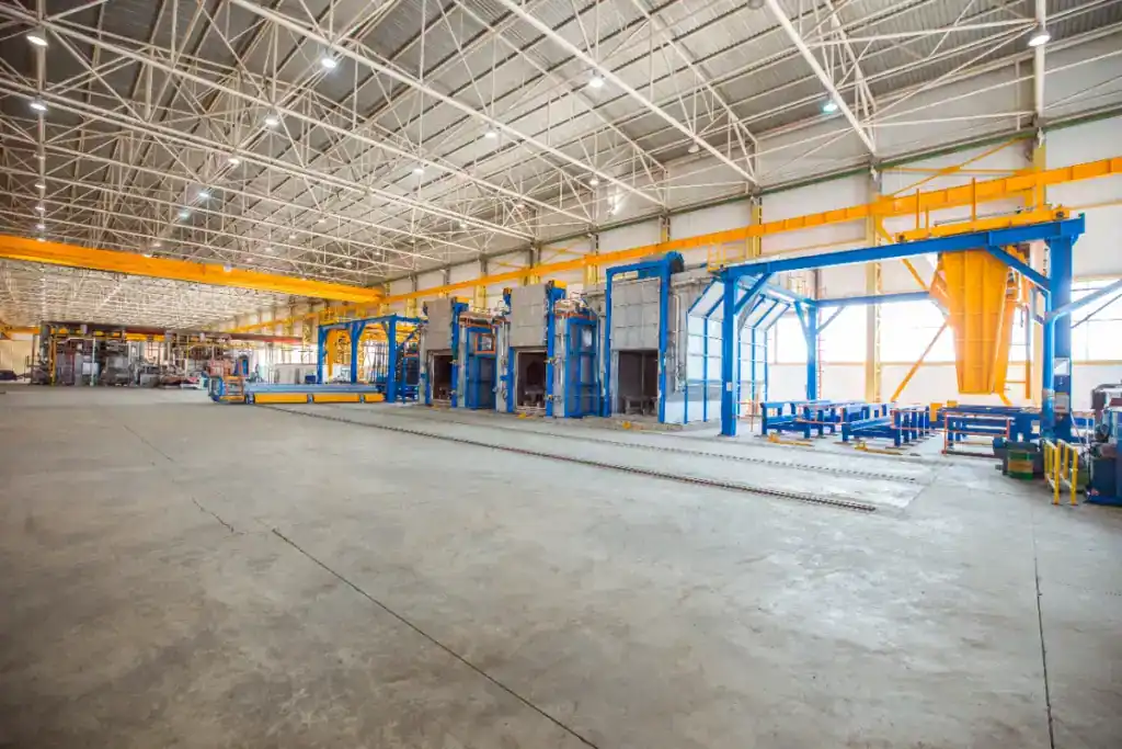 Spacious industrial warehouse with high ceilings, large machinery, and overhead crane systems, ideal for manufacturing or storage purposes.
