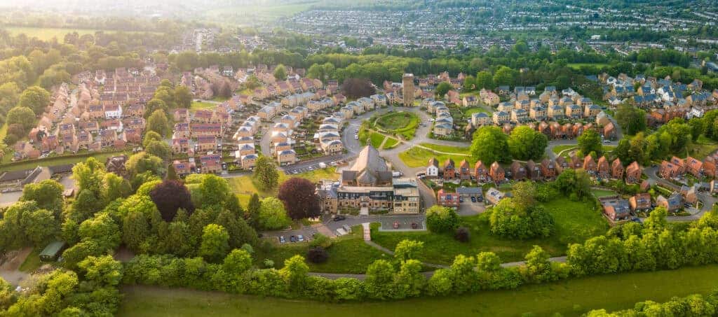 Aerial view of a suburban neighbourhood with a circular street layout, surrounded by lush green trees and well-planned houses, showcasing property development and community living in the UK.