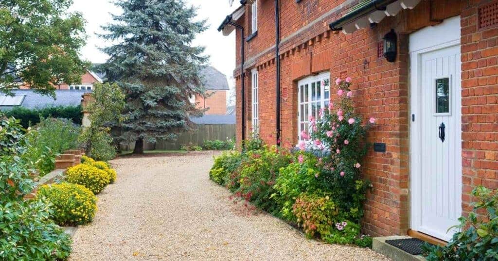 Pathway leading to a charming brick house with colourful garden, perfect for property improvements and landscaping projects.