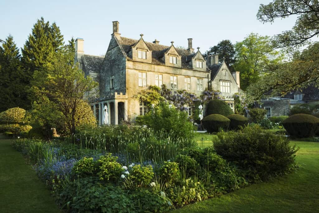 Lush historic manor house surrounded by beautifully landscaped gardens and flowering plants, showcasing luxurious property features.