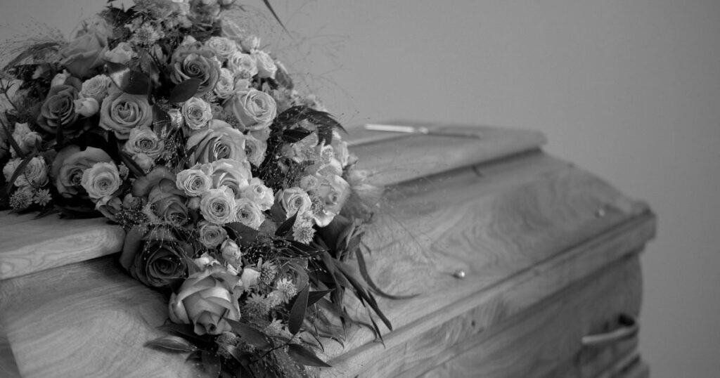 Roses and floral arrangement on wooden casket with Wedding or funeral flowers in black and white image.