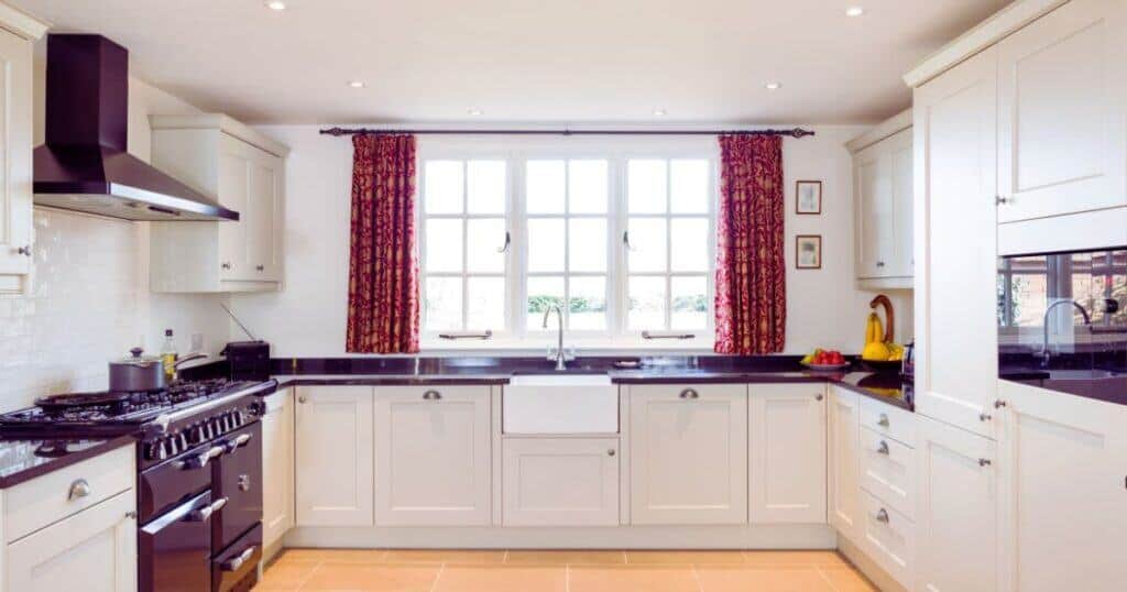 Bright modern kitchen with white cabinets, black countertops, and a large window with red curtains, showcasing property renovation and interior design services.