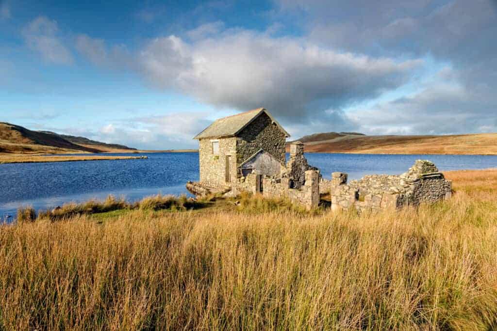 Ruined stone cottage near a lake in a scenic rural landscape, ideal for property restoration projects.