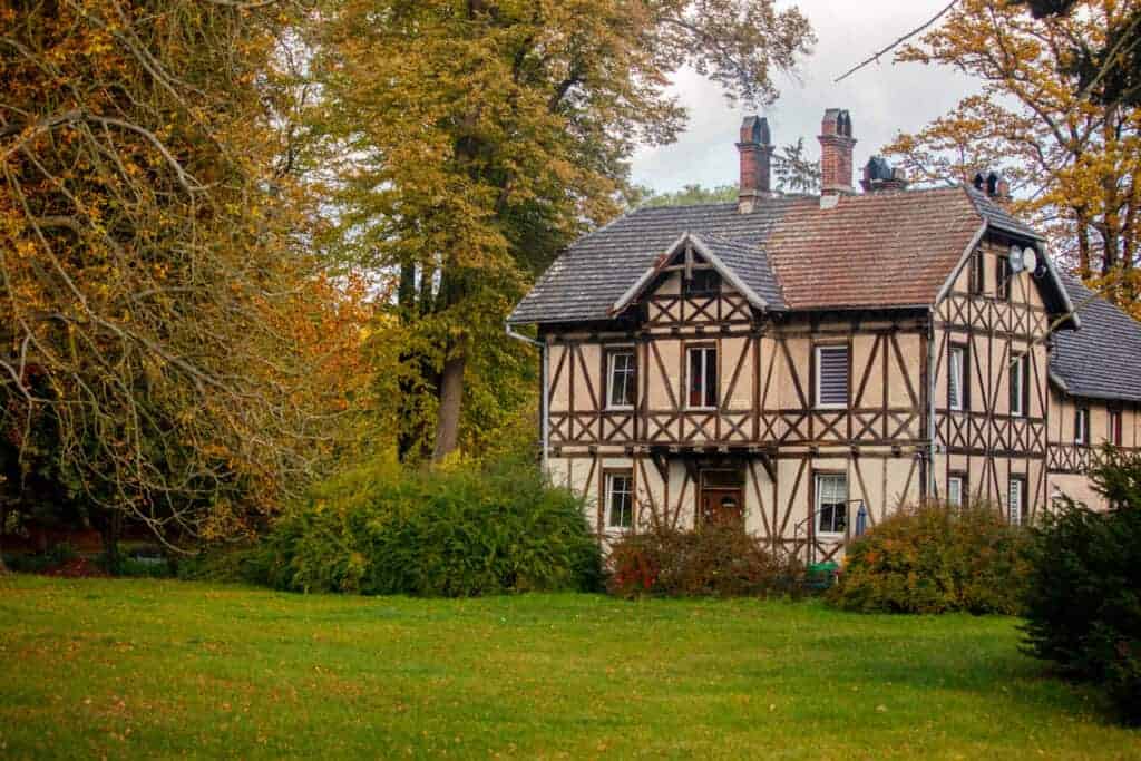Charming half-timbered cottage with autumn foliage, surrounded by lush greenery and trees, showcasing a quaint rural setting.