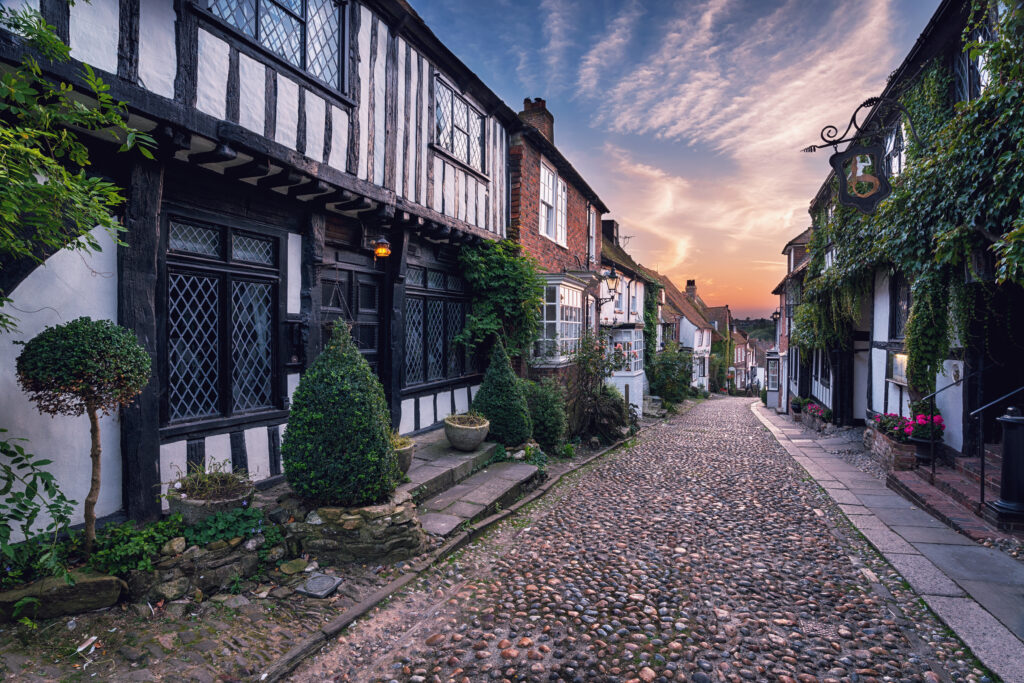 Cobblestone street lined with historic Tudor-style houses at sunset in a charming neighbourhood, showcasing traditional architecture and quaint village ambiance.