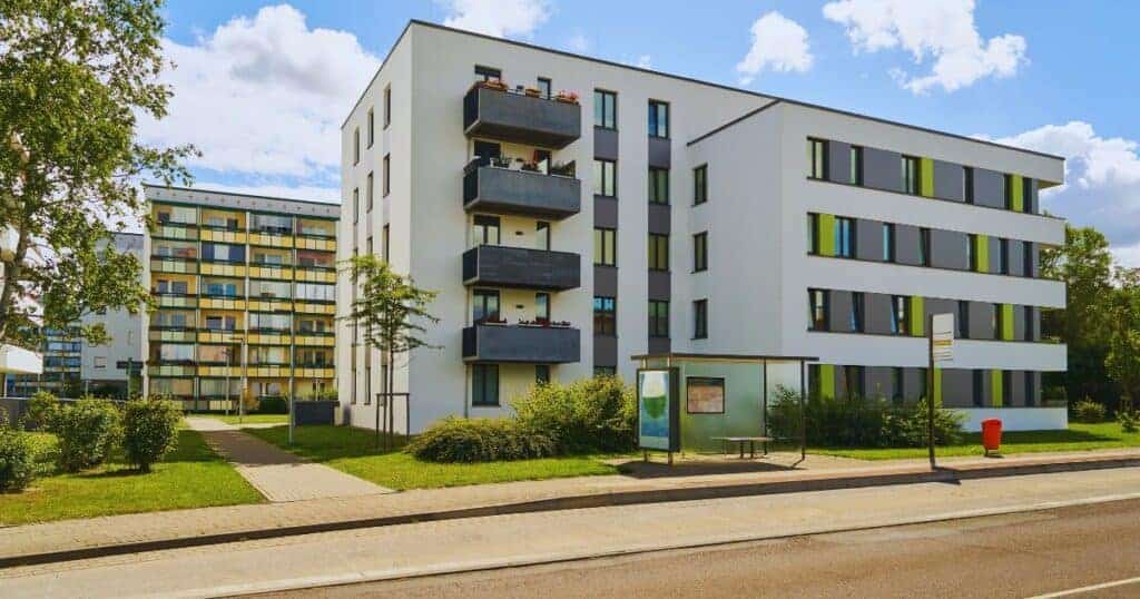 Modern white residential apartment building with colourful balcony accents in a suburban area, sunny day with clear blue sky, part of Property Saviour property management services.