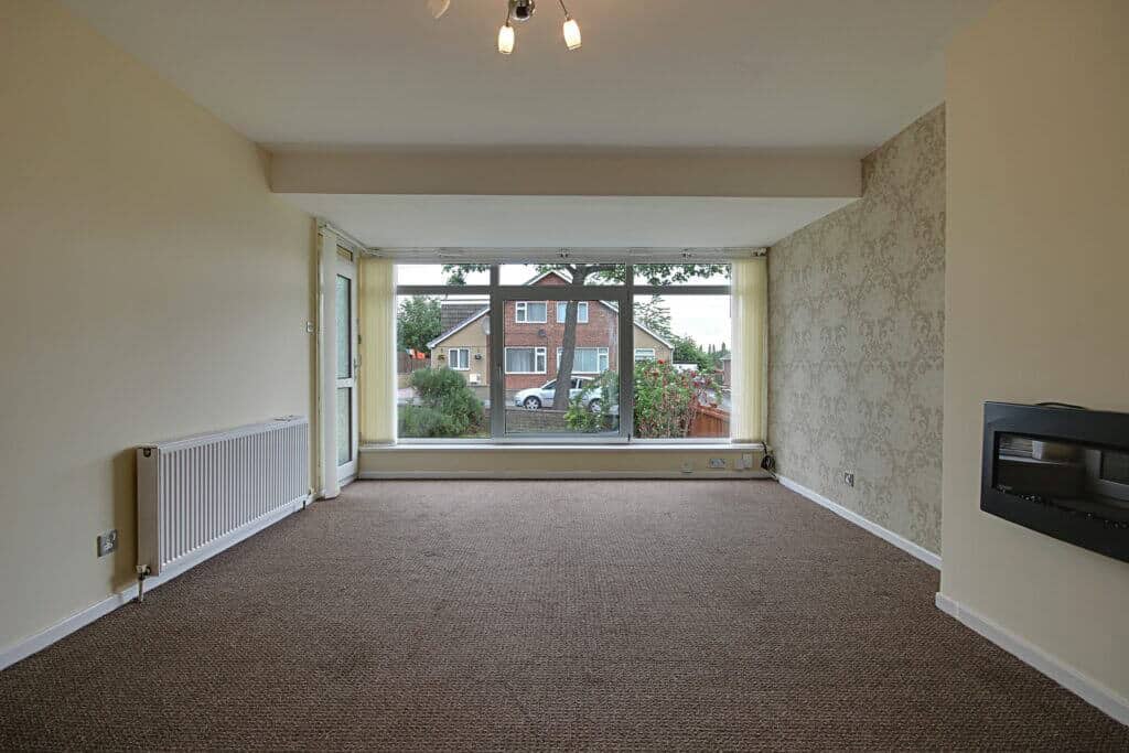 Bright living room in a residential property showing large window with view of neighbouring houses, with neutral colour scheme and wall-mounted fireplace – Property Saviour.