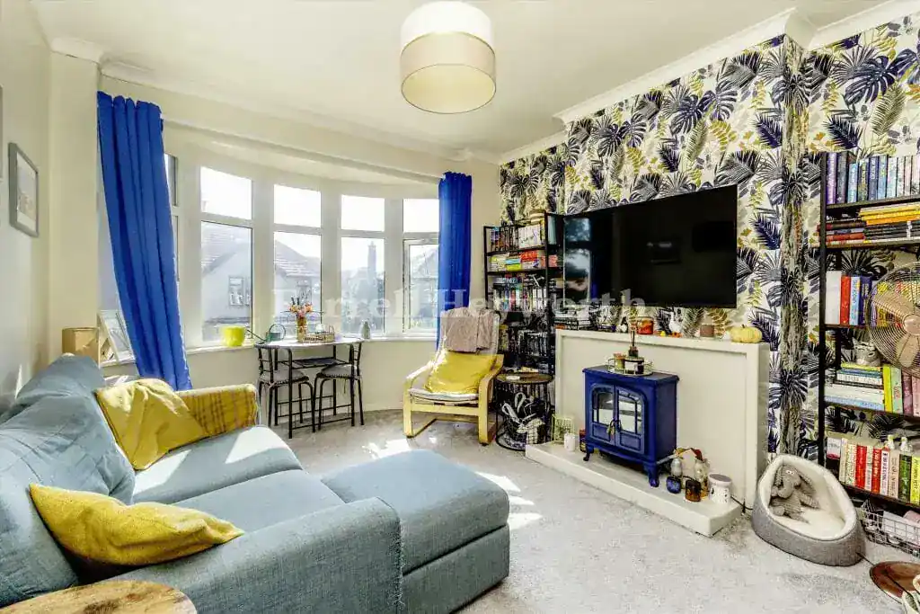 Bright living room with a large window, colourful cushions, and a TV setup.