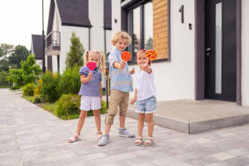 Children holding colourful lollipops in front of a contemporary house, highlighting the idea of young ownership and family living.