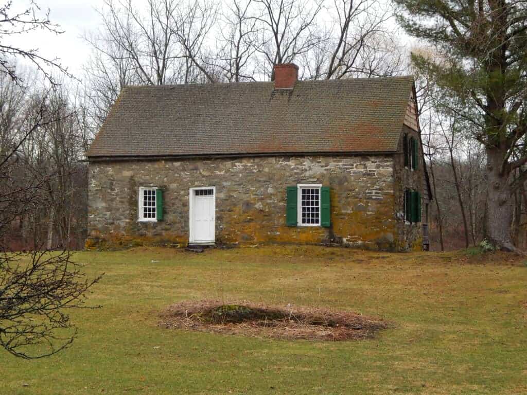 A quaint stone cottage with green shutters, situated in a peaceful rural setting, ideal for buyers interested in traditional homes.