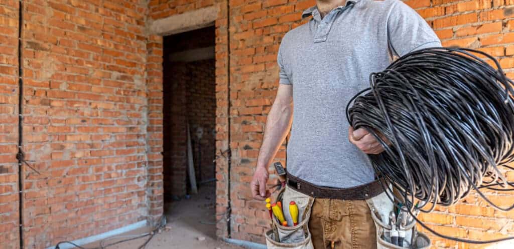 High-quality electrician at construction site holding black electrical cables, working on wiring installation, brick wall background, professional electrical service, property renovation, property saviour.