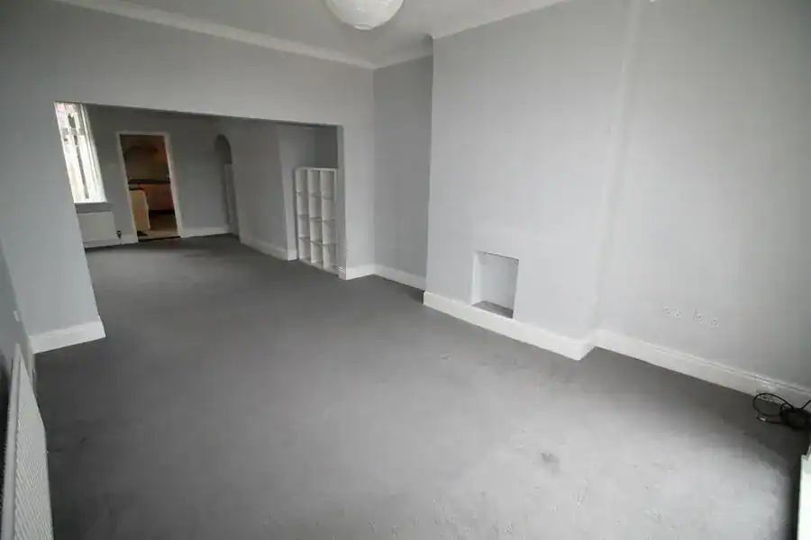 An empty, well-lit living room with grey carpet flooring and white walls, ideal for homebuyers exploring affordable properties in England.