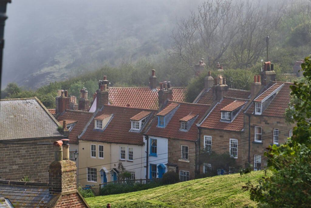 A row of traditional terraced houses with chimneys on a misty hillside, showcasing a quaint neighbourhood ideal for quick house clearance.