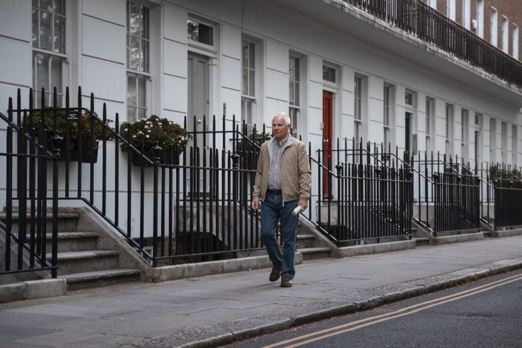 Man walking past a row of white terraced houses with black iron railings, illustrating estate agent fee payments and property management.