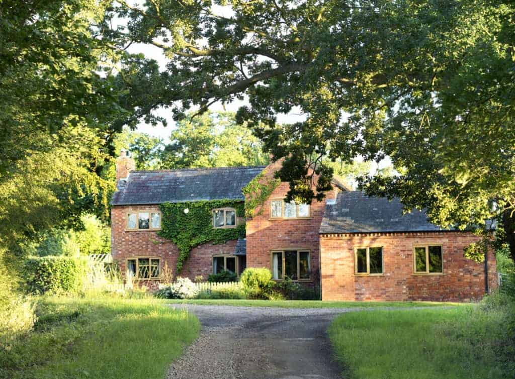 1. Traditional red brick house with lush green ivy and mature trees in the countryside, ideal for property sold or property rescue in the UK.