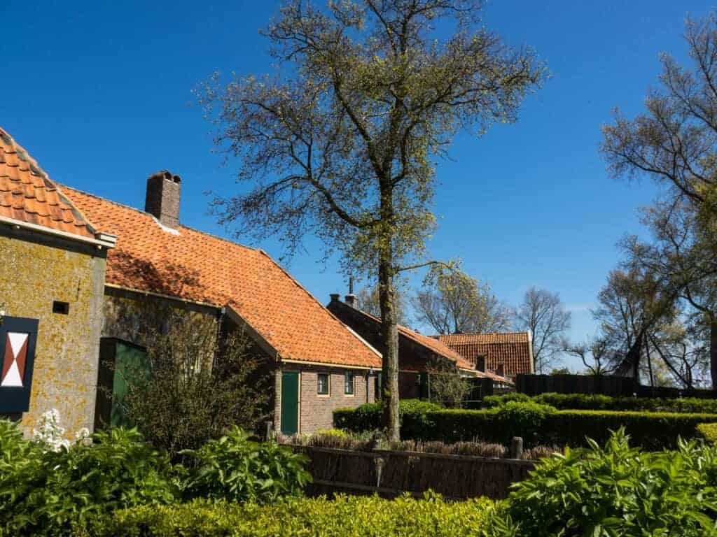 Quaint village houses with red-tiled roofs, surrounded by lush greenery and trees against a clear blue sky.