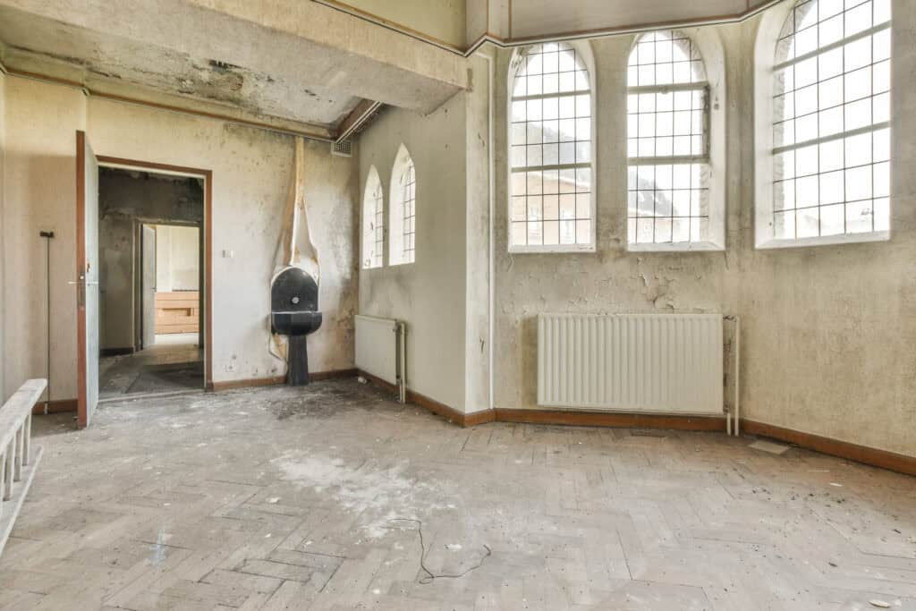 Dilapidated interior of a historic property with peeling walls, large arched windows, and exposed structure, showcasing renovation potential for property saviour services in the UK.