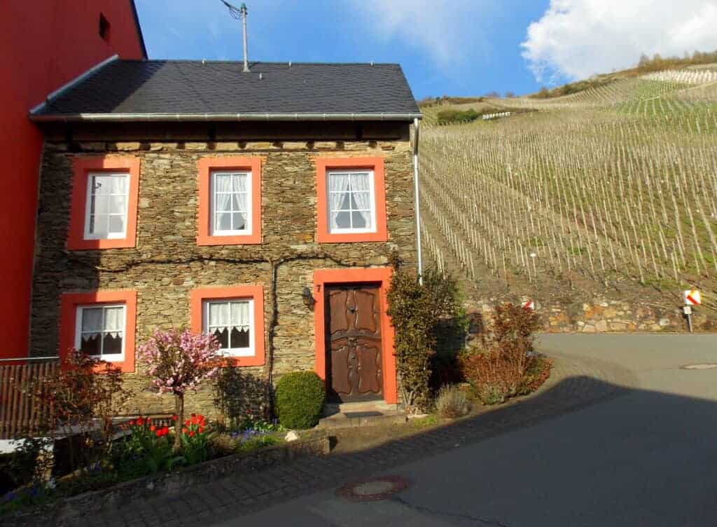 Charming stone house with vibrant orange window frames, nestled on a quiet street near vineyards, showcasing historic architecture and scenic rural landscapes in a picturesque location.