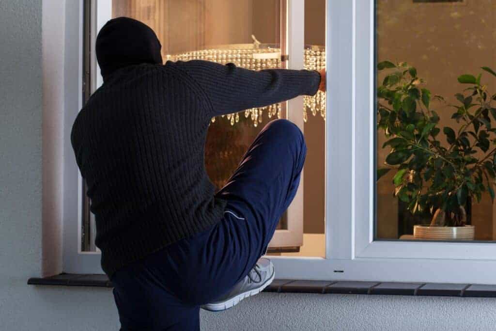 A burglar attempting to break into a home through a glass door, highlighting the importance of home security measures.