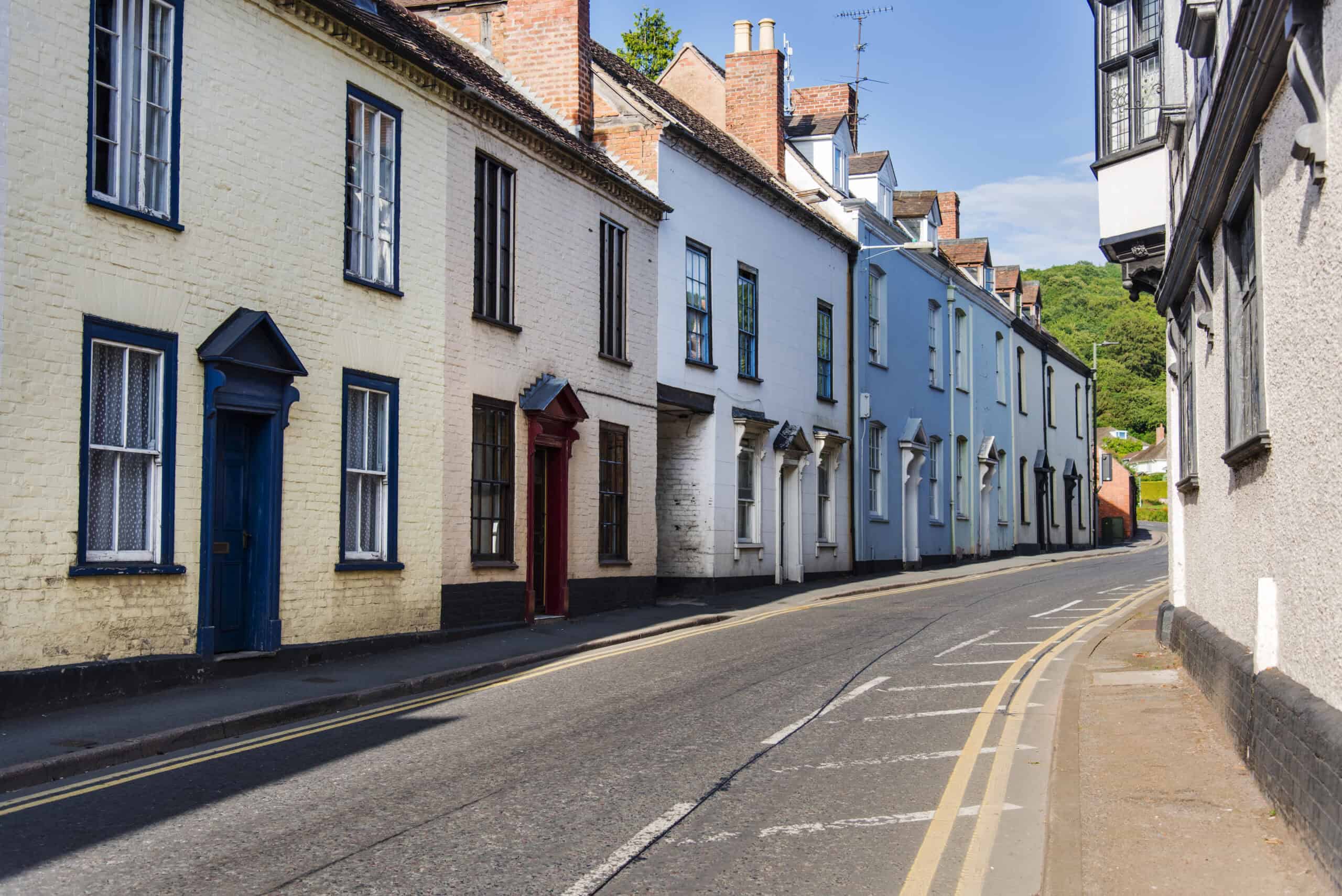 Colourful historic terraced houses in a charming street, showcasing traditional architecture and vibrant doors, set against a scenic hillside backdrop. Ideal for property investment and renovation projects.