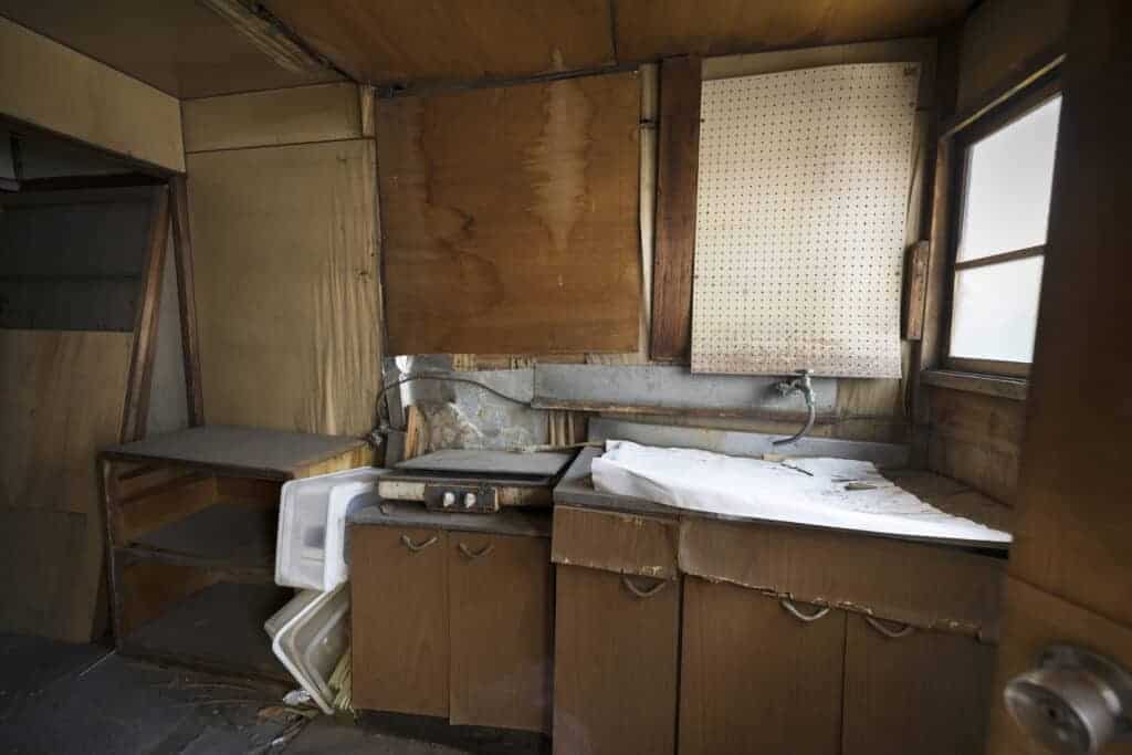 Old, deteriorated kitchen with peeling cabinets, broken countertops, and water damage, showcasing the need for property remediation and restoration services to restore its condition.