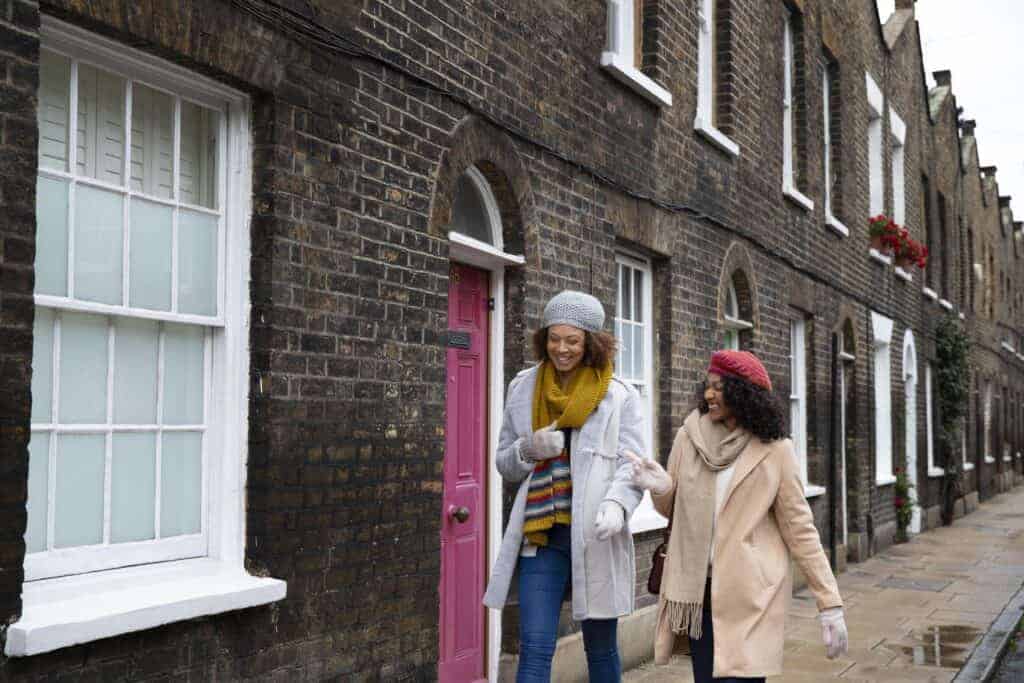 Lively women walking past attractive traditional brick terraced houses, showcasing property value and character, ideal for property maintenance and sales in UK residential areas.